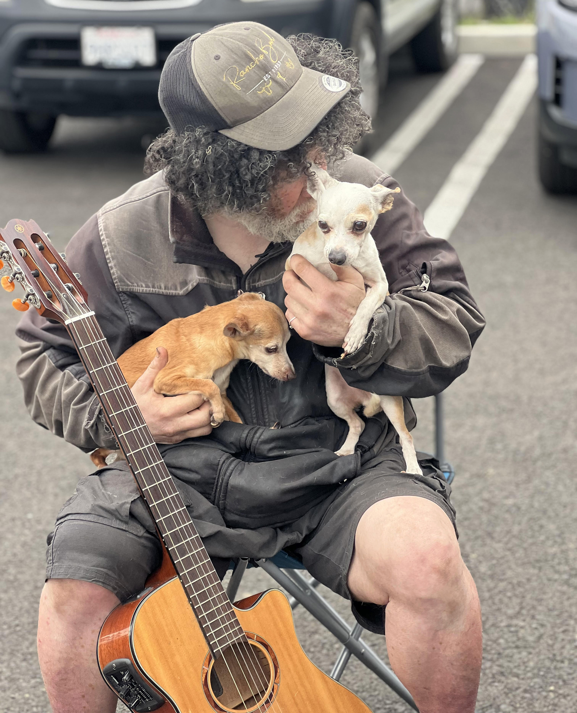 Man nuzzling one of his two dogs with a guitar resting on his leg